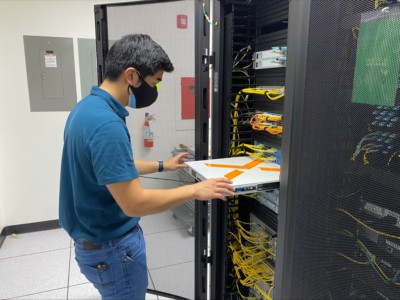 A male inserts a piece of equipment into a server rack