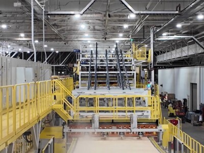 A shot of the inside of a plywood manufacturing facility. Metalwork and walkways criss-cross through the scene as plywood makes its way down the line.